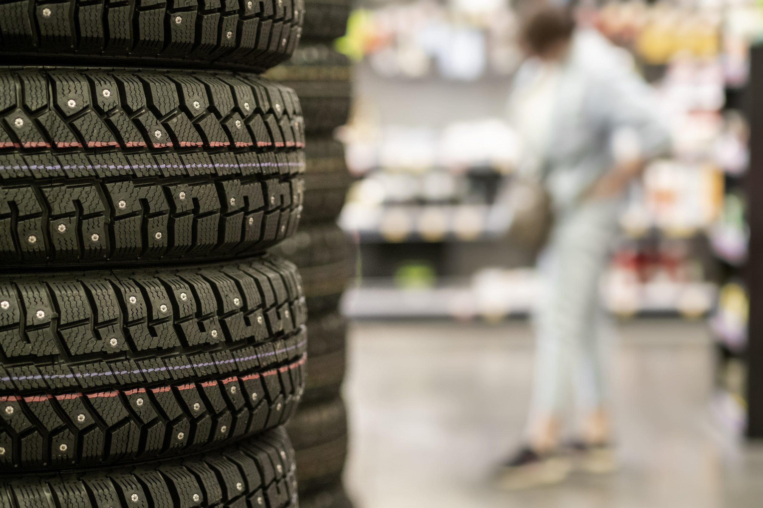 Pilha de pneus novos expostos em loja de revenda de pneus com cliente desfocada ao fundo